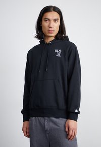 Hoodie noir en coton avec une poche kangourou, des cordons de serrage et un logo graphique sur la poitrine. Texture douce et coupe standard. Marque Nike sur la manche.