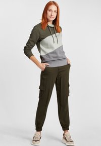 Felpa color blocco verde oliva e grigio con cappuccio, coulisse e polsini a coste, abbinata a pantaloni cargo verde oliva con tasche laterali.