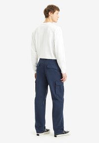 Navy cargo pants with multiple side and back pockets, cotton material, and a relaxed fit, paired with a white long-sleeve shirt and black sneakers.