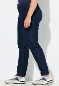 Tmavě modré džíny s úzkým střihem, které mají středně vysoký pas a klasické zadní kapsy, spárované s multibarevnými sportovními botami.