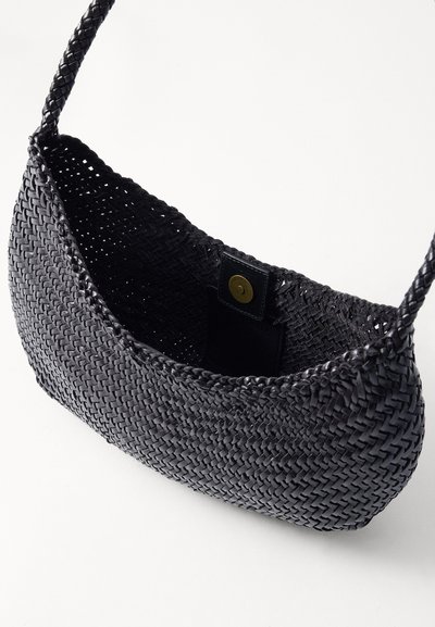 Μαύρη υφασμάτινη τσάντα με υφή, χαρακτηριστική στρογγυλή μορφή και μία λαβή. Το εσωτερικό διαθέτει μια μικρή δερμάτινη ετικέτα με στρογγυρό κουμπί.