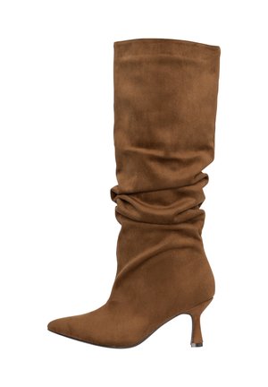 Stivale marrone in pelle scamosciata alta fino al ginocchio, con punta appuntita, gambale morbido e tacco basso a gattino su sfondo bianco.