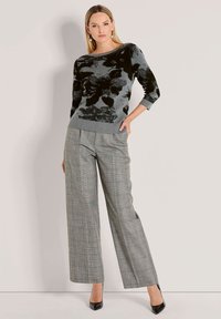 Schwarz-blumiges Muster auf einem hellgrauen gestrickten Pullover, kombiniert mit weit geschnittenen, grauen Karohosen und schwarzen High Heels.