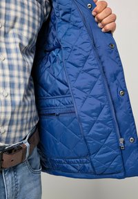 Blå quiltet jakke med en skinnende, tekstureret finish; har trykknapper, lynlåslomme og en indvendig foret foring.