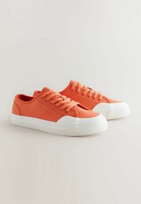 Baskets en toile orange avec semelles en caoutchouc blanc, dotées d'un bout rond, de six œillets et d'un tissu texturé pour une meilleure adhérence et un confort accru.