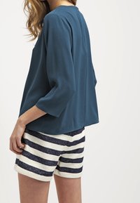 Turkusowa, luźna bluzka z rękawami trzyczwartowymi w połączeniu z białymi i granatowymi szortami w paski, wykonanymi z teksturowanej tkaniny.