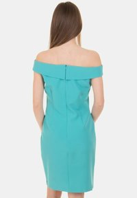 Abito teal off-the-shoulder con un design aderente, chiusura con zip sul retro e texture liscia. Presenta tasche laterali e pince per dare forma.