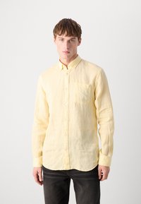 Light yellow, long-sleeve button-up shirt in linen fabric with a chest pocket and button-down collar, worn with dark jeans.