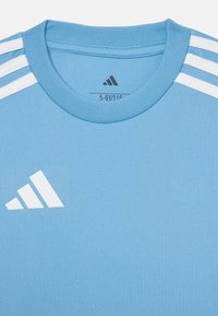 Camiseta deportiva Adidas de color azul claro con acentos en blanco de tres rayas en los hombros y logo de Adidas en el pecho, tamaño 5-6 años.