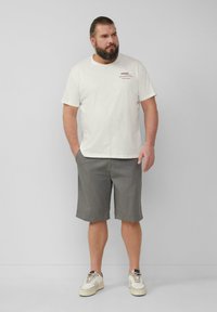 T-shirt en coton beige clair avec impression à l'avant, assortie à un short gris à mi-cuisses et des baskets blanches avec des accents beiges.
