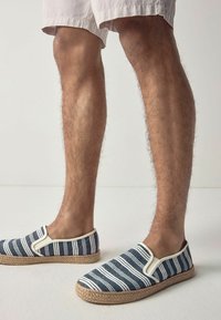 Gestreepte blauwe en witte espadrilles met een jute zool. De instapontwerp heeft elastische zijpanelen en een gestructureerde stoffen bovenkant.