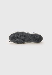 Black rubber shoe sole with textured grip pattern and white side edges; features a pointed toe and slight curvature.