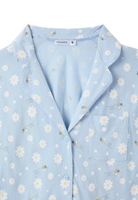Pigiama blu chiaro con motivi di margherite e api bianchi. Presenta un colletto, una tasca sul petto e chiusure a bottone. Tessuto morbido.