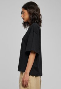 Laisvai krentanti juoda medvilninė marškinėliai su apvalia iškirpte ir trumpomis rankovėmis, derinami su smėlio spalvos plačiomis kelnėmis. Paprastas, švarus dizainas.