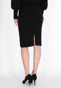 Schwarzer Bleistiftrock mit einem Schlitz hinten, aus weichem Stoff gefertigt. Kombiniert mit schwarzen High-Heels, die ein schmales Design und helle Sohlen haben.