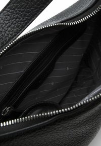 Borsa a tracolla in pelle nera con chiusura a zip. L'interno presenta una fodera in tessuto a righe e una tasca con zip per l'organizzazione.