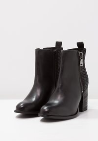 Botines negros con exterior de cuero liso y un patrón texturizado similar a serpiente en la parte posterior. Tienen un cierre lateral y un tacón grueso.