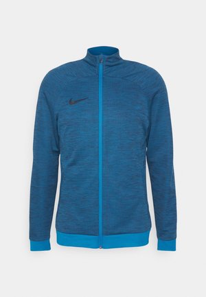 Blaues Zip-Jackett aus strukturiertem Stoff mit Stehkragen. Besitzt kontrastierende blaue Akzente und ein dezentes schwarzes Logo auf der Brust.