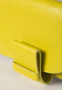 Cartera de cuero amarillo con acabado texturizado, con cierre de solapa curva y letras en relieve. Se pueden ver detalles de costuras a lo largo de los bordes.