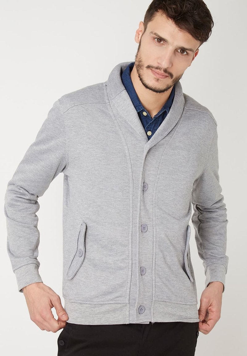 Cárdigan de punto gris con cuello de chal, cierre delantero de cinco botones, dos bolsillos planos y puños acanalados. Textura suave y diseño moderno y casual.