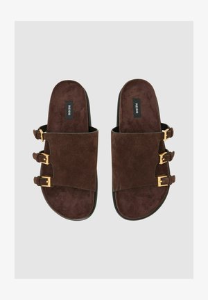 Barna nubuk bőr csúsztatós szandál három aranyszínű csattal, lapos fekete talppal és puha tapintású felülettel. Egyszerű, minimalista kialakítás.