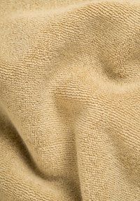 Beige Stoff mit einer weichen, strukturierten Oberfläche, die kleine, dichte Schlaufen aufweist. Das Material wirkt plüschig und fällt geschmeidig.