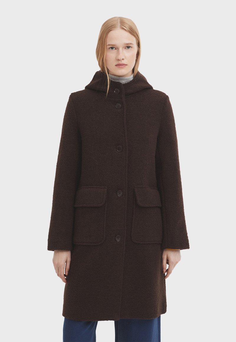 Manteau en laine marron avec une capuche, deux poches avant et une fermeture à boutons. Présente un tissu texturé et une silhouette droite.