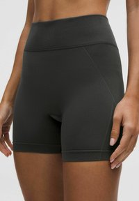 Juodi sportiniai šortai su aukštu šonkaulinio audinio juosmeniu, lygia tekstūra ir plokščiomis siūlėmis. Turi priglundančią išvaizdą ir subtilų geometrinį raštą.
