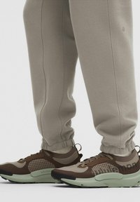 Beige joggingsbroeken gecombineerd met bruine en beige Lululemon sneakers met gevoerde mintgroene zolen.