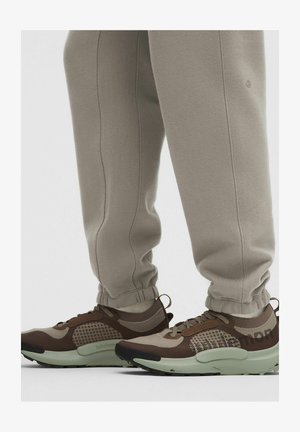 Pantaloni jogger beige abbinati a sneakers Lululemon marroni e beige con suole verdi menta imbottite.