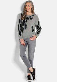 Hellgrauer Pullover mit schwarzen Leopardenflecken, kombiniert mit grauen Hosen und schwarzen Sneakers. Strukturiertes Material und entspannte Passform.