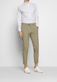 Pruhovaná bílá a světle modrá košile na knoflíky; slim-fit béžové kalhoty; bílé tenisky. Hladká tkanina, zakázkový design a moderní střih.