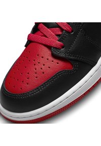 Černé kožené tenisky s červenými akcenty, vybavené perforovanou špičkou, texturovanými červenými a černými panely a bílou mezipodešví. Červené tkaničky.