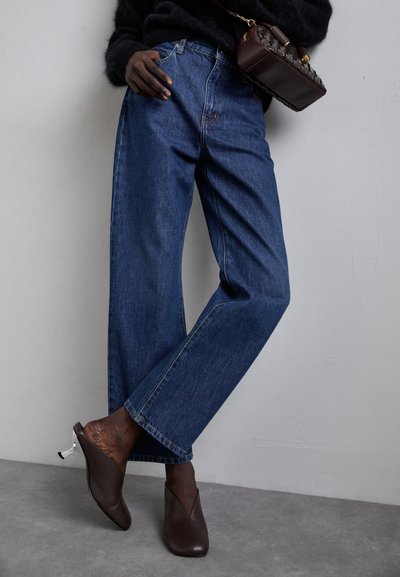 Blauwe denim jeans met een losse pasvorm, met een middelhoge taille en rechte pijpen. Gecombineerd met donkergroene leren muiltjes met zilveren accenten.