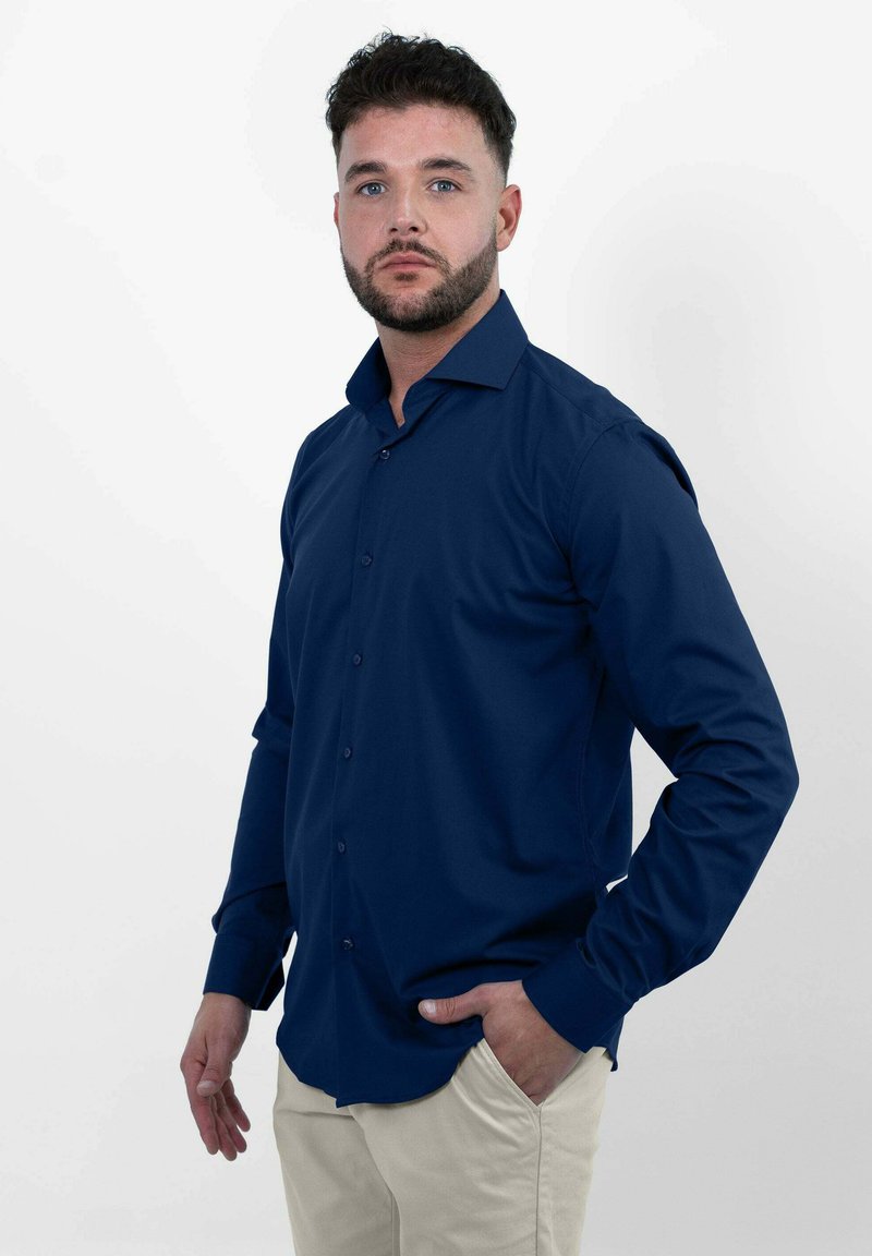 Donkerblauwe blouse met lange mouwen en knopen, voorzien van een kraag, met een gladde textuur en een getailleerd silhouet, gedragen met lichtbeige broek.