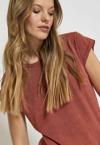 T-shirt textured color ruggine con maniche corte arrotolate, caratterizzato da una vestibilità comoda e scollatura rotonda, indossato da un modello con capelli lunghi.