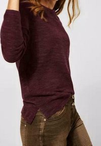 Bordeaux gestreepte langwerpige trui met een geribbelde textuur en zijsplitten, gecombineerd met olijfgroene geblokte broek met zichtbare knopen.