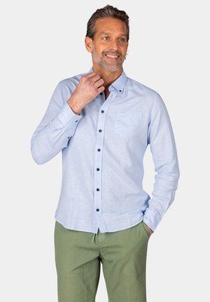 Lichtblauw overhemd met knoopsluiting, gemaakt van zacht stof, met een borstzak, donkere knopen en een groene logo-accent. Draagt met groene shorts.