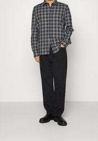 Camisa de botones a cuadros en blanco y negro con mangas largas, combinada con pantalones sueltos negros y botas de tobillo negras.