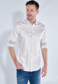 Helles graues kurzärmliges Hemd mit Knopfverschluss, das über ein gestreiftes Manschetten-Detail und eine Brusttasche verfügt. Hergestellt aus glattem Stoff.