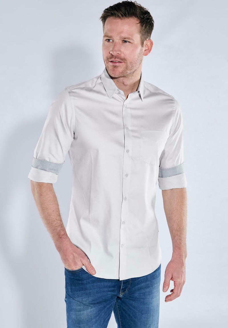 Helles graues kurzärmliges Hemd mit Knopfverschluss, das über ein gestreiftes Manschetten-Detail und eine Brusttasche verfügt. Hergestellt aus glattem Stoff.
