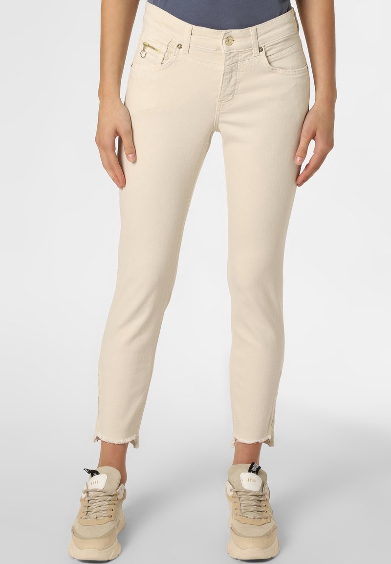 Jean beige taille haute avec une silhouette ajustée, doté d'une poche zippée et d'un ourlet effiloché, assorti à des baskets de couleur claire.