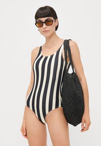 One-piece swimsuit with vertical black and cream stripes, made of stretchy material. Features wide straps and a high-cut leg design.