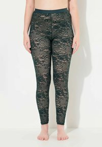 Kantleggings in donkergroen met bloemenpatronen. Ze hebben een hoge tailleband en een aansluitend ontwerp, dat de ingewikkelde kanttexturen toont.