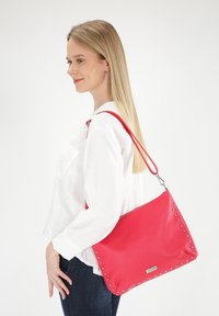 Rote Lederhandtasche mit silbernen Nietenakzenten. Verfügt über einen einzigen verstellbaren Tragegurt und einen Reißverschluss oben. Rechteckige Form.