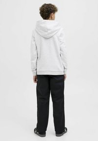 Felpa grigia con un ampio cappuccio e polsini a coste, abbinata a pantaloni neri larghi e sandali neri. Design semplice e funzionale.