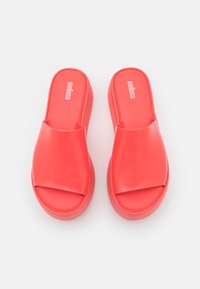 Röda slip-on sandaler med en blank yta, bred rem och rund tå, tillverkade av flexibelt material med en slät textur.