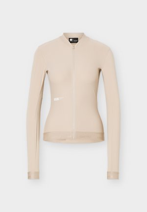 Beige long-sleeve fitted cycling jersey with full front zipper and subtle logo on the left side and cuffs.