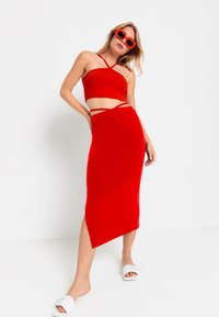 Rode twee-delige set met een aansluitende crop top met kruislingse banden en een knielange rok met een zijsplit. Soepele stoftextuur.