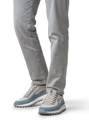 Grijze spijkerbroek gecombineerd met sneakers in meerdere tinten lichtgrijs en blauw. De sneakers hebben gestructureerde overlays, dikke veters en robuuste zolen.